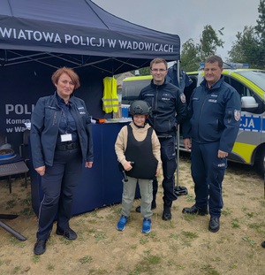 Dwóch policjantów i policjantka oraz chłopiec ubrany w elementy policyjnego umndurowania