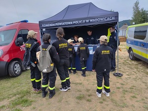 Policyjny namiot gdzie stoi policjantka i dwóch policjantów oraz grupa młodzieży wokoło