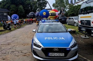 Oznakowany radiowóz, w tle kolarze i kibice