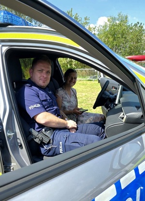 W radiowozie siedzi policjant oraz kobieta w stroju cywilnym