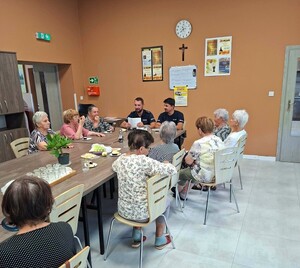 Przy stoliku siedzi dwóch policjantów, a wokoło seniorki