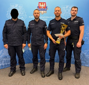 Na zdjęciu czterech umundurowanych policjantów, pierwszy ma zamazana twarz, a trzeci trzyma puchar