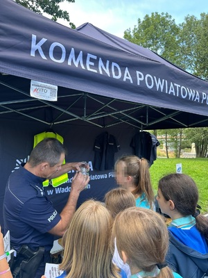 Przed namiotem policjant i grupa osób