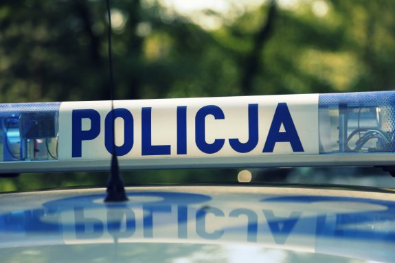 Sygnały świetlne i dźwiękowe na dachu pojazdu. Na białym tle niebieski napis Policja, po prawej i lewej stronie światła koloru niebieskiego