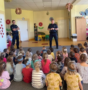 Dwóch umundurowanych policjantów, przed nimi dzieci siedzące na dywanie