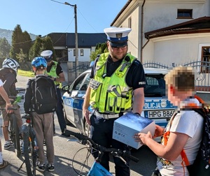 Dzieci na rowerach i dwóch policjantów. Jeden z nich przekazuje chłopakowi kask