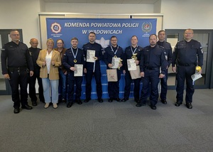 Dziewięciu policjantów, z których czterech trzyma dyplomy i medale. Między nimi kobieta i mężczyzna w stroju cywilnym.