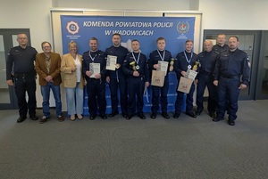 Dziewięciu policjantów z medalami i pucharami oraz kobieta i mężczyzna w stroju cywilnym. W tle baner policyjny.