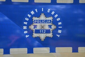 Na niebieskim tle odznaka policyjna koloru szarego z napisem Policja 112, wokoło napis Pomagamy i chronimy