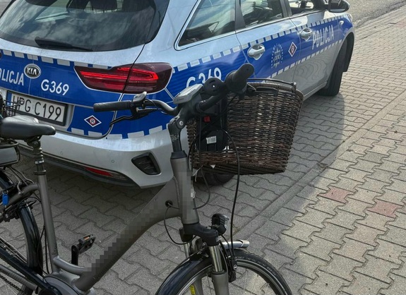 Na tle oznakowanego radiowozy rower z koszykiem na kierownicy