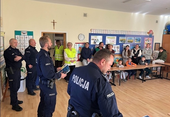 Na zdjęciu czterech policjantów, dwie osoby w kamizelkach odblaskowych oraz dorośli i dzieci