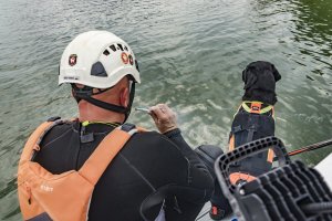 Siedzący tyłem i patrzący w wodę przewodnik i pies ratowniczy