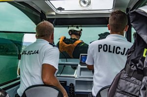 Dwóch umundurowanych policjantów siedzących w łodzi, na dziobie widać przewodnika psa z psem ratowniczym