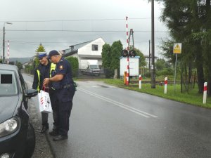 Umundurowany funkcjonariusz ruchu drogowego oraz Straży Ochrony Kolei stojący obok samochodu, trzymający w ręku ulotki