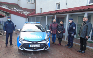 Oznakowany radiowóz corolla. Po lewej stronie stoi Komendant Komisariatu Policji w Andrychowie, po prawej Komendant Powiatowy Policji w Wadowicach, Burmistrz Andrychowa z Zastępcą oraz Wójt Gminy Wieprz.