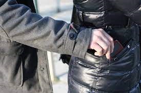 Na zdjęciu widać rękę osoby, która wyciąga portfel z kieszeni płaszcza