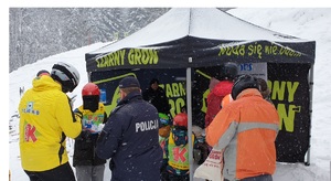 Na stoku narciarskim, przed namiotem z napisem Czarny Groń grupa narciarzy, dzieci i dorośli oraz umundurowani policjanci.