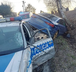 Miejsce kolizji, zderzenie oznakowanego radiowozu i samochodu marki audi koloru niebieskiego. W tle karetka