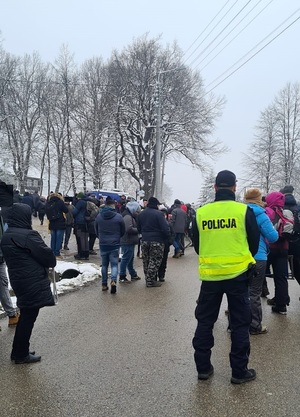 Umundurowany Policjant w kamizelce odblaskowej z napisem Policja. Wokół tłum osób.