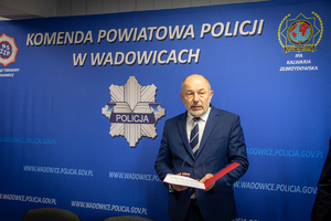 Wójt Gminy Lanckorona Tadeusz Łopata na tle baneru Komenda Powiatowa Policji w Wadowicach