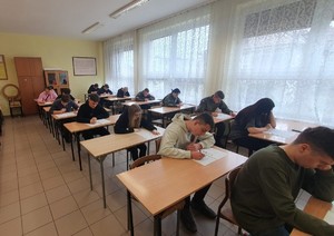 W klasie, w ławkach siedzą uczniowie, którzy rozwiązują test.