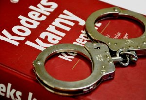 Policyjne kajdanki położone na kodeksie karnym. Kodeks koloru czerwonego z białym napisem Kodeks karny
