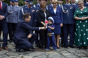 Na zdjęciu grupa osób kobiety i mężczyźni w strojach cywilnych oraz umundurowani policjanci oraz mały chłopiec ubrany w strój policjanta.