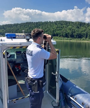 Policjant posterunku wodnego w Świnnej Porębie na łodzi patrolowej obserwuje prze lornetkę tafle wody
