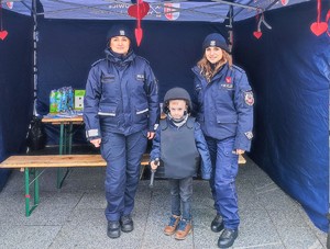 Dwie umundurowane policjantki. Pośrodku stoi mały chłopiec ubrany w elementy umundurowania policyjnego.